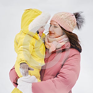 A mother woman holds a toddler baby in her arms, winter snow. Mom e.