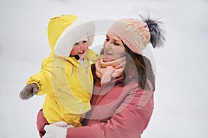 A mother woman holds a toddler baby in her arms, winter snow. Mom e.