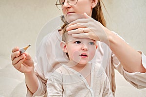 A mother woman measures the temperature of a sick toddler baby wit