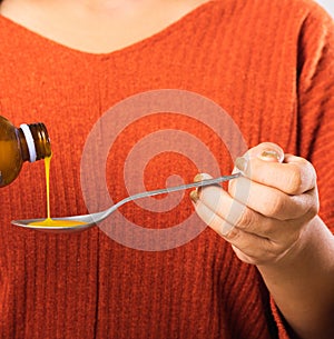 Mother woman pouring liquid medication or antipyretic syrup cough from bottle to spoon