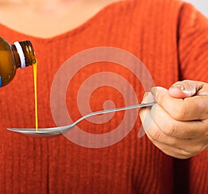 Mother woman pouring liquid medication or antipyretic syrup cough from bottle to spoon