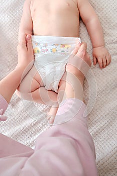 A mother woman puts on a diaper for a baby boy. Mom dresses child in clothes on the bed