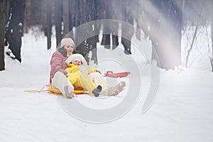 A mother woman with a toddler baby rides an ice sled in a snowy park.