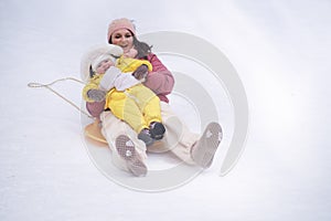 A mother woman with a toddler baby rides an ice sled in a snowy park.