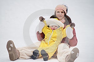 A mother woman with a toddler baby rides an ice sled in a snowy park.
