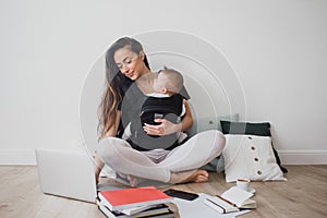 Mother working at home with baby in ergo backpack