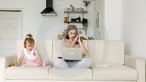 Mother working from home, having a work video call, phone call and child playing nearby. Remote work. Telecommute job