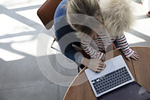 A mother working from home at a laptop computer with her young son on her lap