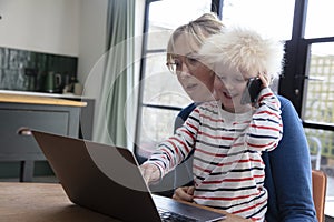 A mother working from home at a laptop computer with her young son on her lap
