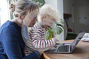 A mother working from home at a laptop computer with her young son on her lap