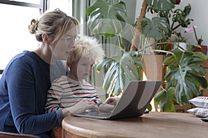 A mother working from home at a laptop computer with her young son on her lap