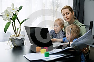 Mother working from home. using laptop at desk with kids on her lap