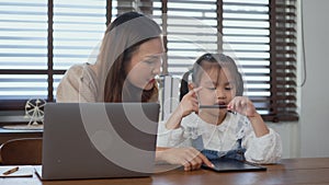 Mother working with laptop computer at home and help daughter doing homework