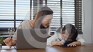 Mother working with laptop computer at home and help daughter doing homework