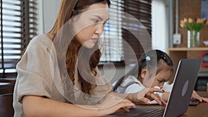 Mother working with laptop computer at home and help daughter doing homework