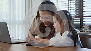 Mother working with laptop computer at home and help daughter doing homework