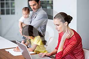 Mother working on laptop with daughter studying photo