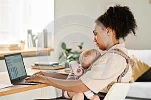 Mother working on laptop at home with baby