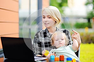 Mother working oh laptop and holding her toddler daughter