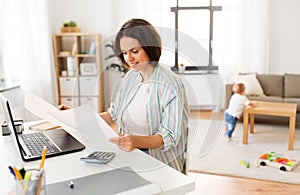 Mother working with papers and baby boy at home