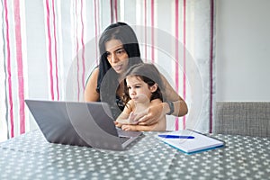 Mother works with computer with her daughter sitting on her lap in the dining room at home photo