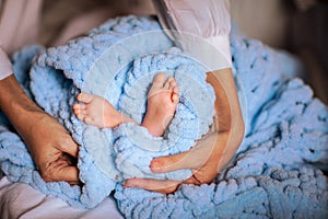 Mother& x27;s hands holding newborn& x27;s feet near soft blue blanket.