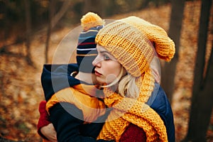 Mother in yellow hat scarf hugging pacifying sad upset crying toddler boy son in autumn fall park outdoor.