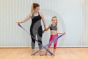 mother yoga instructor and daughter do strenght exercises with elastic band