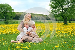 Mother and Young Children Sitting in Flower Meadow Laughing