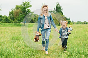 Mother and young daughter hold hands and walk in the meadow