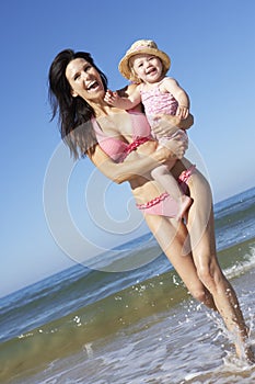 Mother With Young Daughter Running Along Beach Together