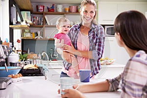 Mother With Young Daughter Talking To Friend In Kitchen