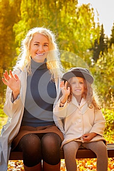 Mother and young little girl with blonde hair in an autumn park on a yellow and orange leaf background. Family walking