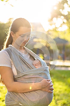 Motherhood, care, infants, summer, parenting concept - Young beautiful mom with a newborn baby in a sling walks and