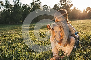 Motherhood and childhood. Happy beautiful young mother lying with her cute daughter on grass in the park. Happy family