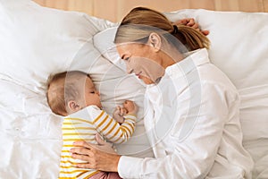 Motherhood lifestyle concept. Happy loving mother lying with sleeping baby girl in bed in bedroom at home, top view