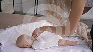 Motherhood, parent plays with baby daughter who is lying on the bed and bitting her fingers at home