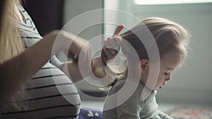 Motherhood, pregnancy, childhood, beauty and health concept - close-up of young cute dark-haired girl combing her little