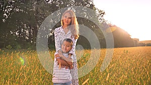 Mothering hug of asian female of her happy son, standing on the wheat field on sunrise