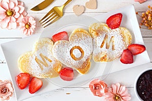 Mothers Day breakfast heart shaped pancakes with MOM letters, top view table scene on white wood