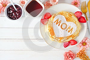 Mothers Day breakfast pancakes with heart shape and MOM letters, above view corner border on a white wood background