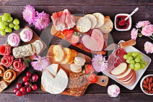 Mothers Day charcuterie table with a dark wood background. Assorted cheese, meat, fruit and sweet appetizers.