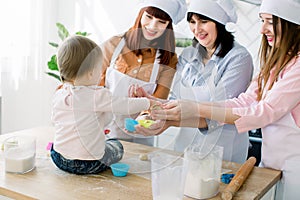 Mothers Day, family, cooking and people concept - little cute baby girl and her mom, aunt and grandmother making and
