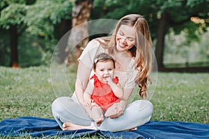 Mothers Day holiday. Young smiling Caucasian mother and girl toddler daughter hugging in park. Mom embracing child baby on summer