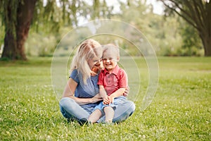 Mothers Day holiday. Young smiling Caucasian mother and laughing boy toddler son sitting on grass in park. Family mom and child