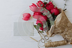 Mothers day. Stylish red tulips bouquet, greeting card, gift, scissors, twine on rustic white wood