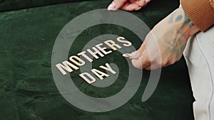 MOTHERS DAYS - word made of wooden letters on the green sofa woman's hands with tattoo concept copy space