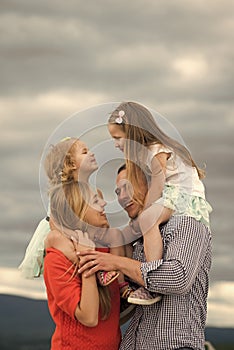 Mothers, fathers day. Children and parents enjoy vacation together. Girls sit on mother father shoulders on cloudy sky