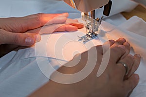 Mothers hands leading daughters hands to sew with a sewing machine