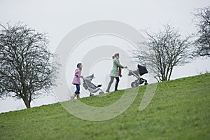 Mothers Pushing Baby Strollers Uphill In Park